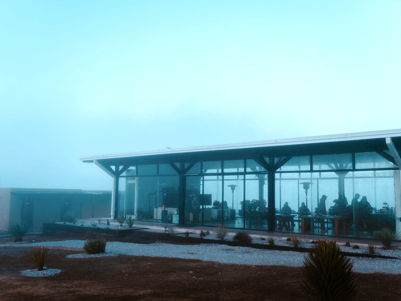 The modern glass-walled Coahuila lodge under a timber roof at dawn, guests dining inside